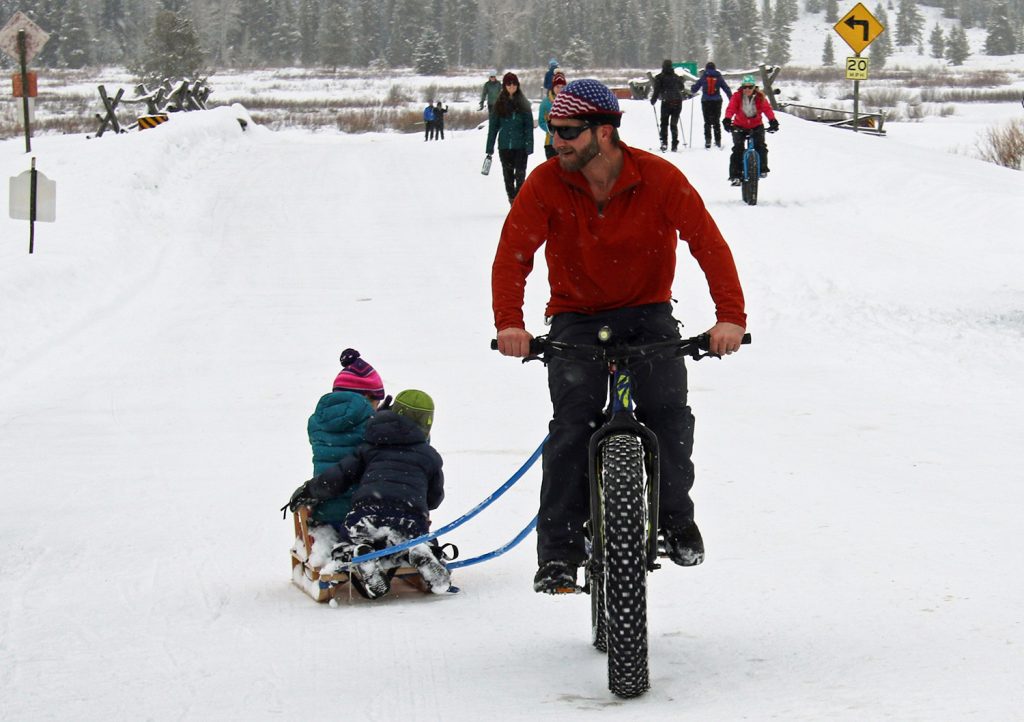 Father towing two kids in a sleigh tethered to his fat bike