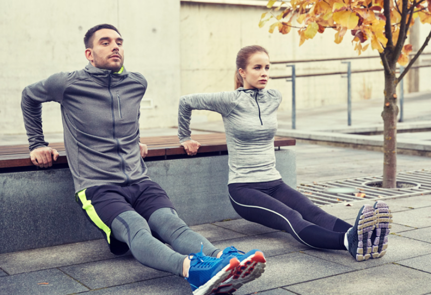 Image of a man and woman doing dips off a park bench