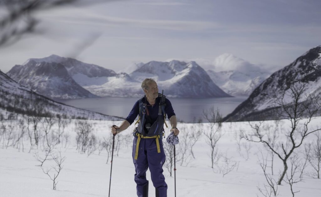 Jim Roscoe, Nordic Ski luminary, in front of a snow covered mountain scene.