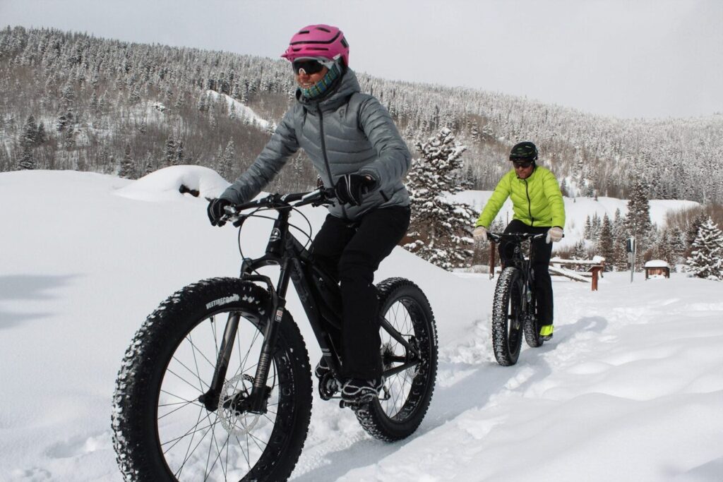 two people ride fat bikes up a snowy hill