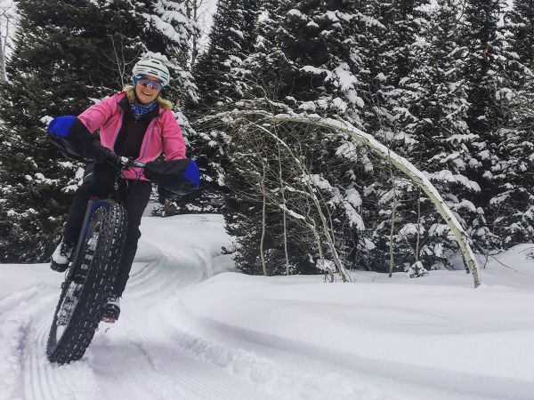 Woman wears a pink jacket and bikes downhill on a fat bike in the snow