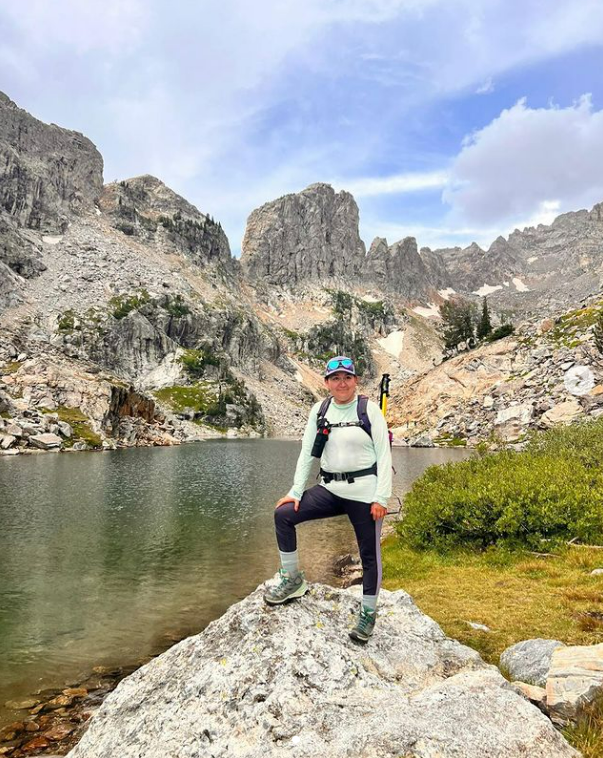 Mirella Susano Garcia stands on a boulder at a mountain summit - Local organization gets Latinx residents outside 