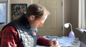 Stacey Barker with pen in hand works on an illustration at his desk.