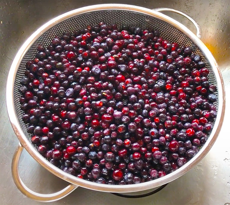 A colander of red-violet huckleberries that are freshly washed 