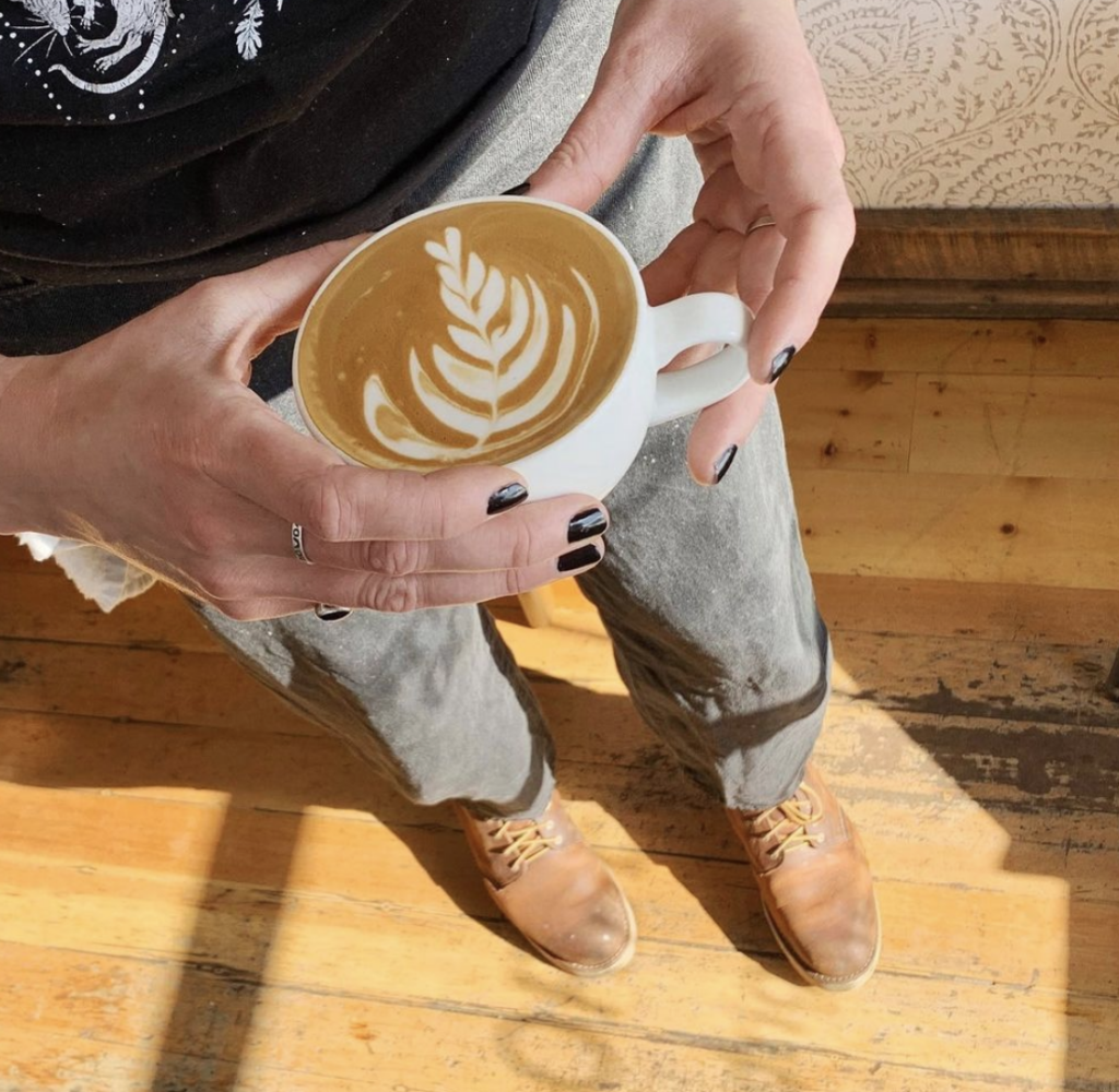 a barista holds a latte with pretty latte art in natural lighting