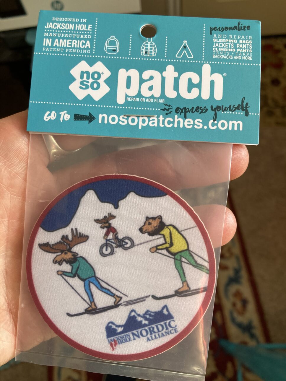A custom JH nordic Noso patch created by Stacey Barker of Barking Goat Studios. A moose and bear cross country ski while another moose skis in the background.