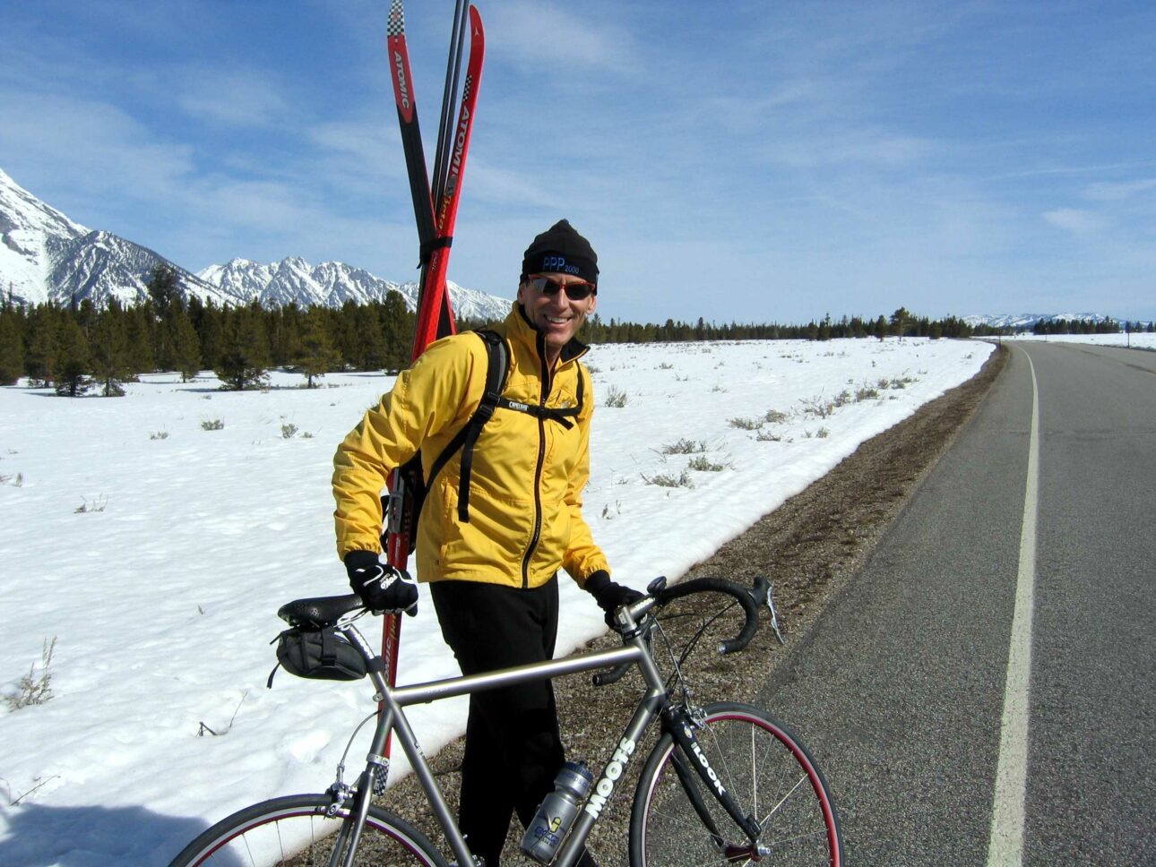 A man with xc skis on his back getting ready to ride his bike