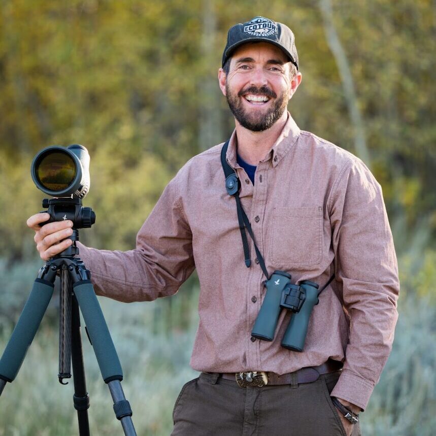 Taylor Phillips of JH EcoTour Adventures poses with camera, tripod, and binoculars.