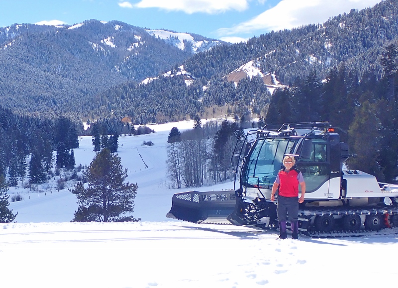 A groomer in a red vest stands outside the ski cat machine near Trail Creek