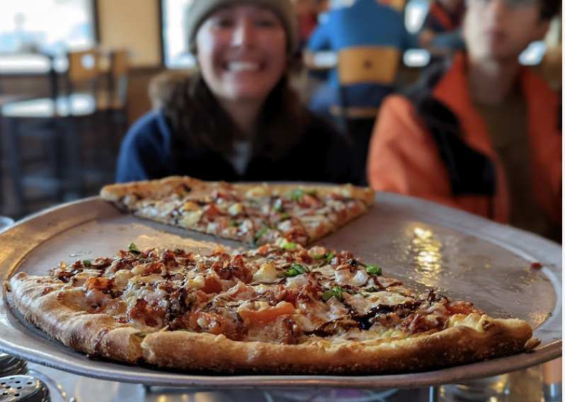 A pizza with a few slices taken from it and a girl in the background