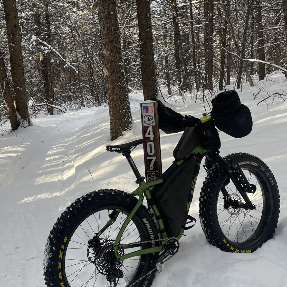A fat bike propped on a USFS trail post near the groomed singletrack in the forest