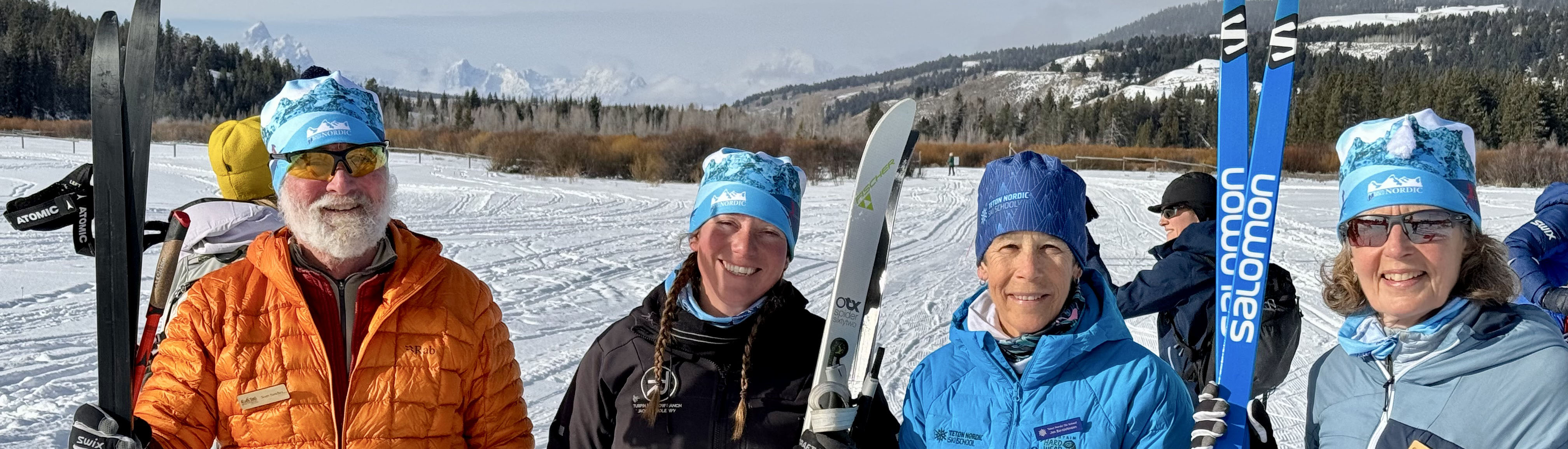 Community partners in action. Four cross-country ski instructors standing on snow with skis, Tetons in the background.