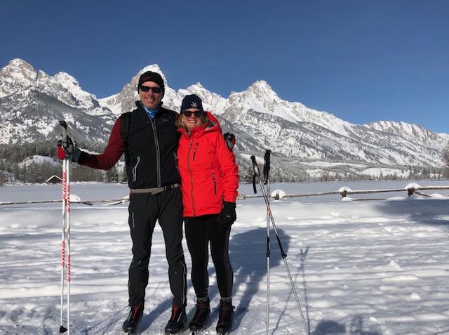 A couple in cross-country gear in front of the Tetons under a blue sky