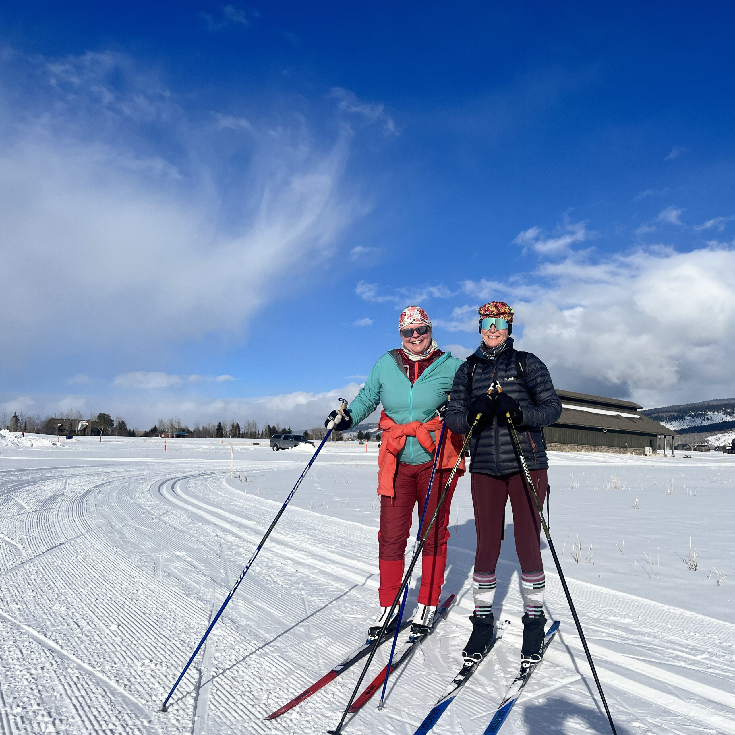 two women facing the camera on skate skis with blue skies